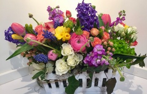 A colorful flower arrangement in a white picket fence vessel